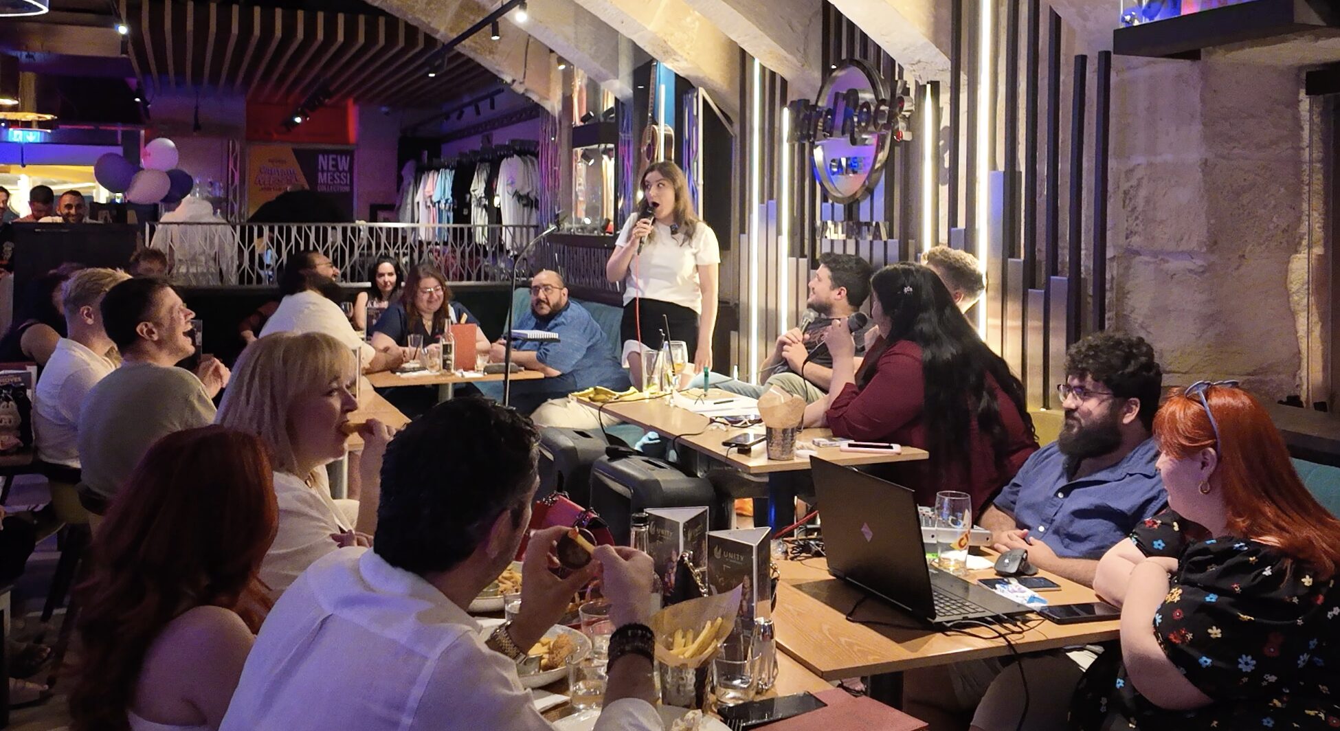 A photo of Cansu Pylkkänen performing stand-up comedy on stage, engaging the audience with humor and energy. The setting is intimate and lively, reflecting the dynamic atmosphere of the show.
